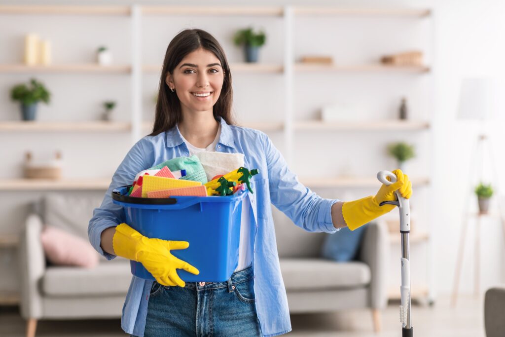 Cheerful young housewife holding bucket with clean
